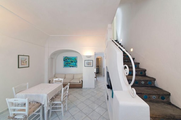Un espace repas comprenant une table et des chaises, un canapé, un escalier avec des marches décoratives et un mur orné de tableaux encadrés.