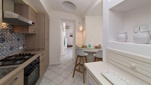 A kitchen with a stove, oven, and patterned backsplash; a dining area with a table and chairs; and a white cabinet with decorative items. - Fantasy House Suites (Forio)