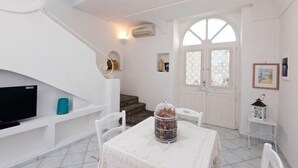 A white interior with a staircase, a table with chairs, a TV, and a birdcage. - Fantasy House Suites (Forio)
