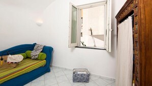 A room with a bed, a window, a wooden cabinet, and a small trash bin. - Fantasy House Suites (Forio)