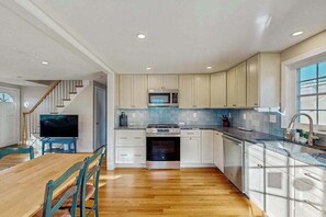 A modern kitchen with white cabinets, a microwave, stove, and a dining area with wooden table and chairs. - Cozy retreat near beaches with washer/dryer, AC, games, patio & yard (Falmouth)