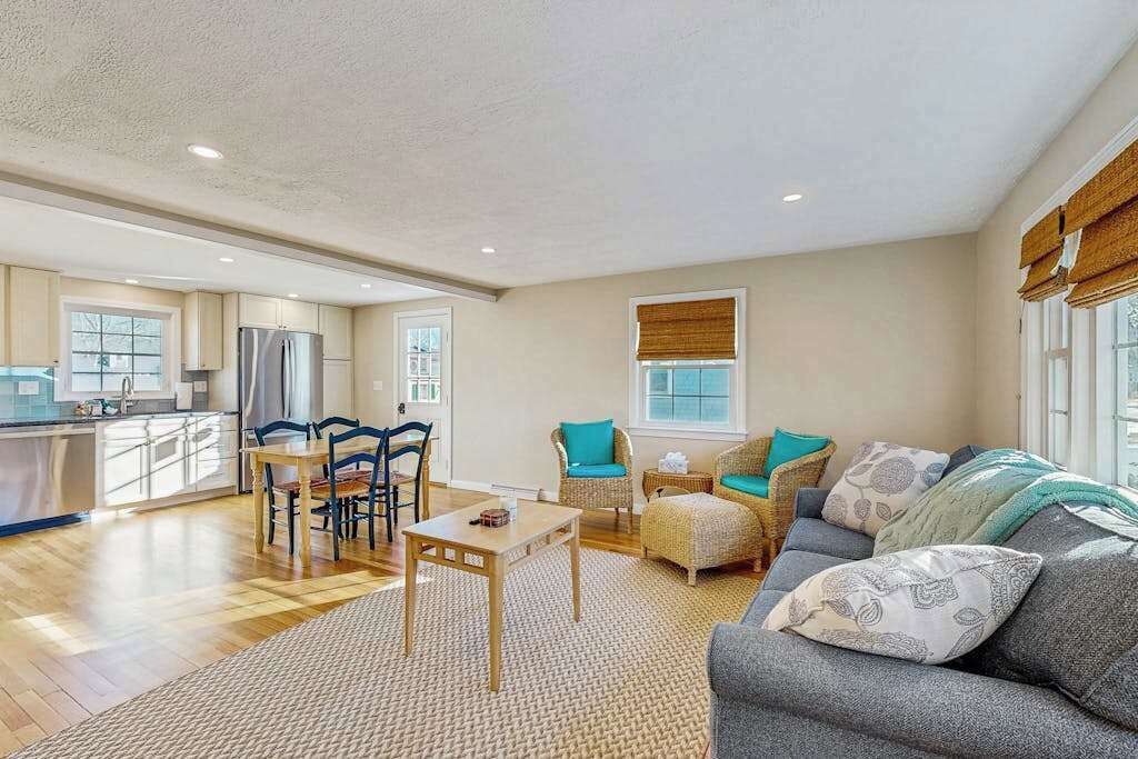 A spacious living area with a sofa, chairs, a dining table, and a kitchen in the background.