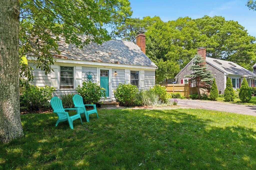 A house with a front porch, a tree, and two green chairs.