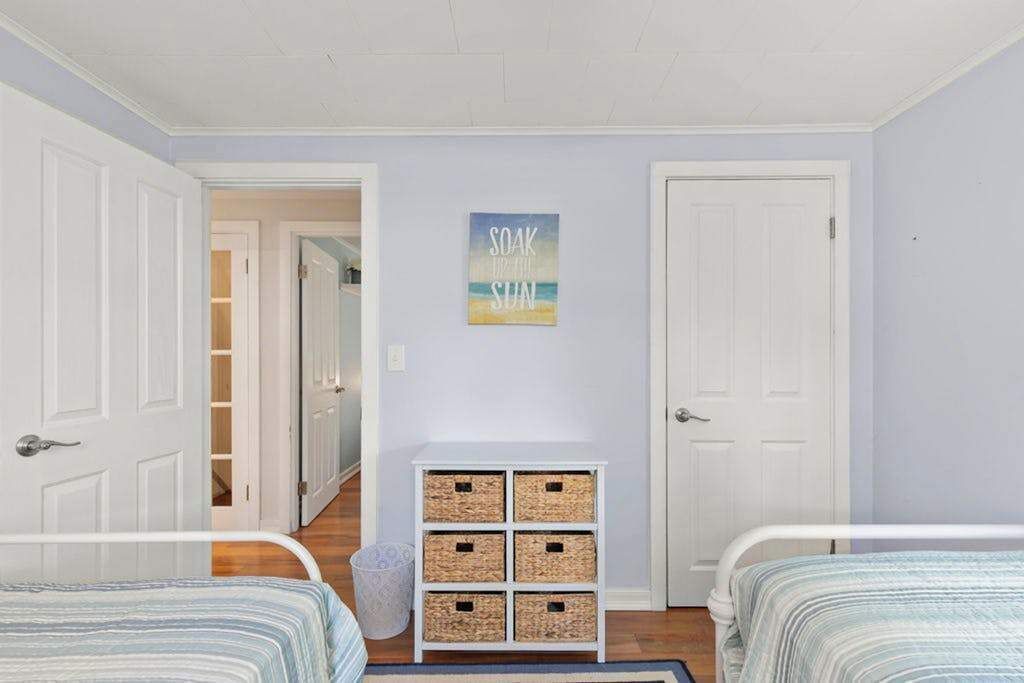 A bedroom with two beds, a hallway, a door, and a wall-mounted basket shelf.