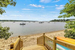 A beach with a wooden deck, boats on the water, and a clear sky. - Peaceful Great Pond getaway with private yard, patio, AC & family-friendly games (Falmouth)