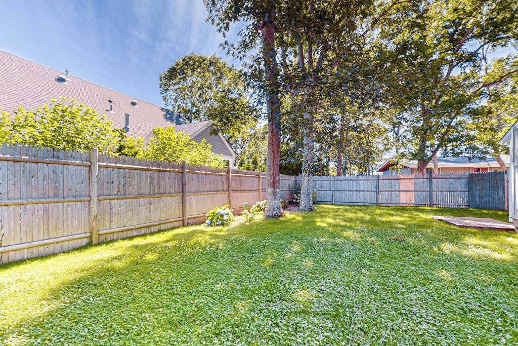Un jardin avec une clôture en bois, un arbre et une pelouse verdoyante.