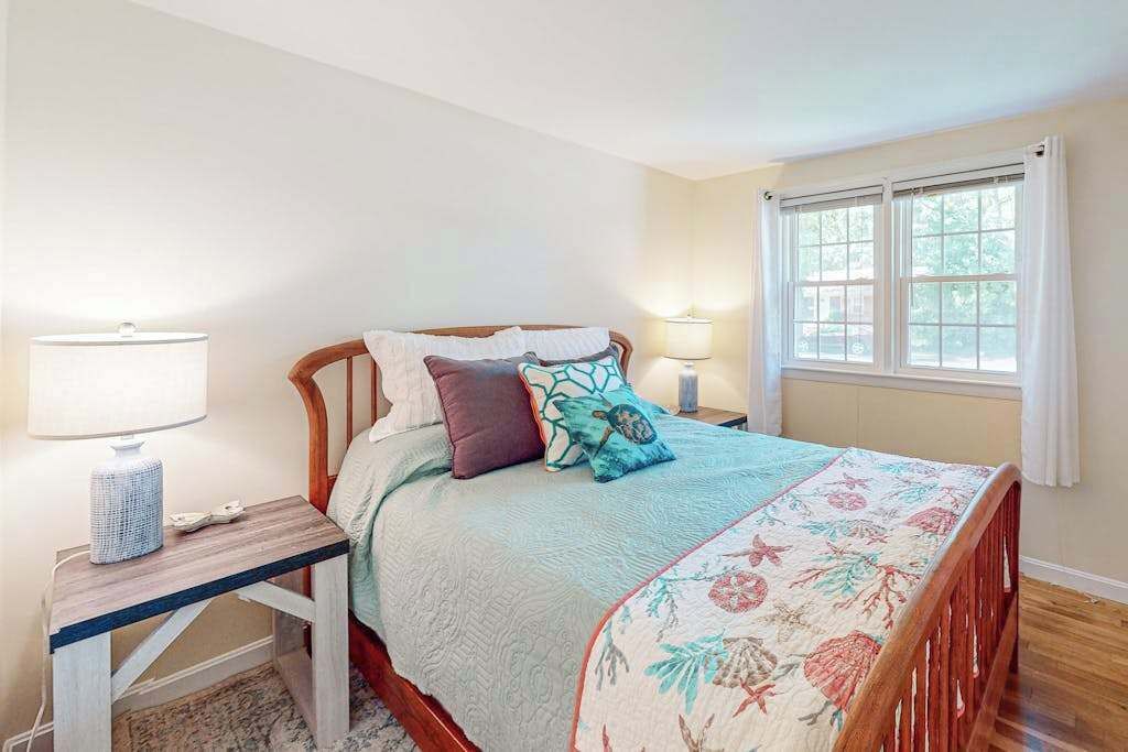 A bedroom with a bed, two bedside tables, a window with curtains, and a lamp on each table.