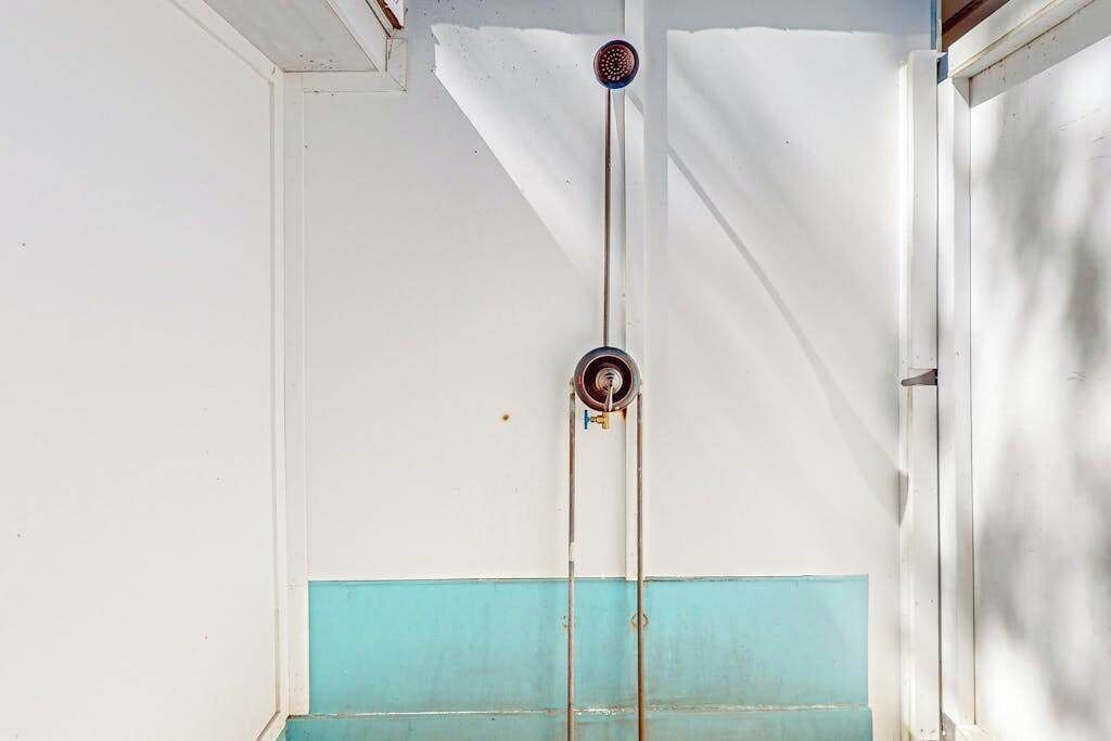 A bathroom with a white and teal color scheme, a shower with a vertical pipe, and a window.