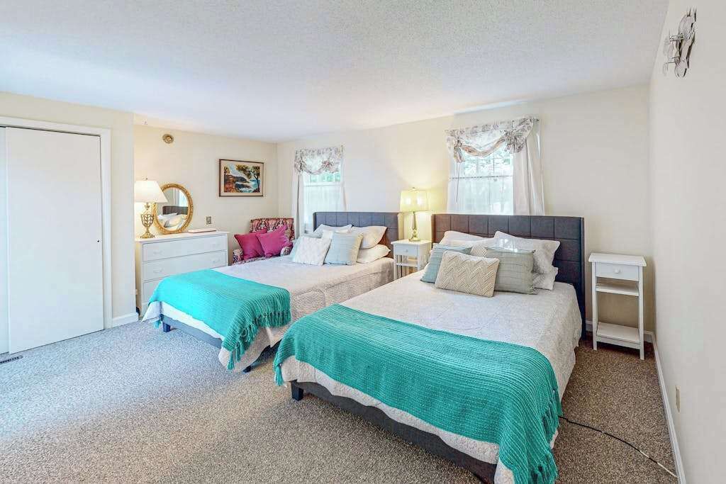 A bedroom with two beds, a dresser, a nightstand, and a window with curtains.