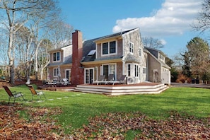 A two-story house with a patio, a chimney, and a lawn with chairs.