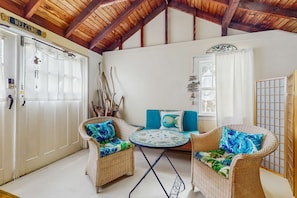 A room with wicker furniture, a round table, and a wooden ceiling.