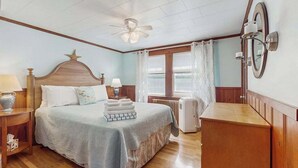 Un dormitorio con cama, ventilador de techo, radiador, cómoda y ventana con cortinas.