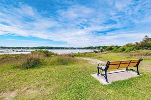 A bench by a grassy area with a view of a body of water and distant land. - Neighborhood charmer with deck, W/D, Outdoor shower, Dog friendly, Wifi (Falmouth)