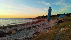 A beach with a blue umbrella, rocky shoreline, and houses in the background. - Our House in West Falmouth | House in Falmouth with private beach access (Falmouth)