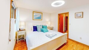 A bedroom with a bed, bedside tables, a nightstand, a ceiling fan, and a door. - Our House in West Falmouth | House in Falmouth with private beach access (Falmouth)