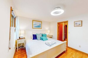 A bedroom with a bed, bedside tables, a nightstand, a ceiling fan, and a door. - Our House in West Falmouth | House in Falmouth with private beach access (Falmouth)