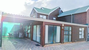 Un edificio moderno con amplios ventanales, una zona de estar al aire libre techada y un camino pavimentado.