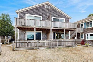 A two-story wooden house with a balcony, a garage, and a gravel driveway. - Central Ptown condo:  steps to beach, walk to town, trails & entertainment (Provincetown)