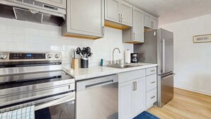 Uma cozinha moderna com eletrodomésticos de aço inoxidável, armários brancos e um tapete azul.