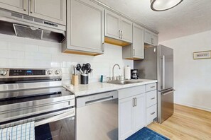 A modern kitchen with stainless steel appliances, white cabinetry, and a blue rug. - Central Ptown condo:  steps to beach, walk to town, trails & entertainment (Provincetown)