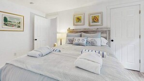 Quarto com cama, duas portas, cabeceira e duas imagens emolduradas na parede.