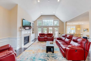 A spacious living room with a fireplace, red leather sofas, and a large window. - Modern home with dog-friendly yard, private pool/hot tub, pickleball & fast WiFi (Mashpee)
