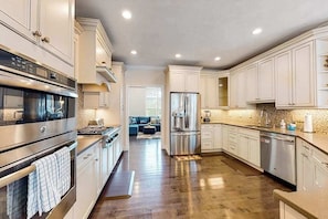 A modern kitchen with stainless steel appliances, white cabinetry, and a wooden floor. - Modern home with dog-friendly yard, private pool/hot tub, pickleball & fast WiFi (Mashpee)