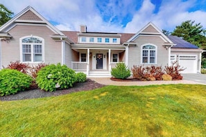A two-story house with a front porch, a garage, and a well-maintained lawn. - Modern home with dog-friendly yard, private pool/hot tub, pickleball & fast WiFi (Mashpee)