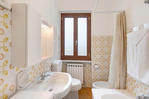 Et badeværelse med to håndvaske, toilet og et vindue over toilettet.