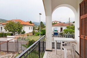 En balkon med et bord og stole, udsigt til omkringliggende huse og et metalhegn.