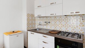 Una cucina con mobili bianchi, un piano cottura a gas, un lavello e un piccolo frigorifero.