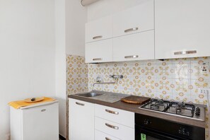 Eine Küche mit weißen Schränken, einem Gasherd, einer Spüle und einem kleinen Kühlschrank.