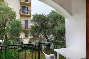 En balkon med et hvidt bord og stole, omgivet af grønt og en bygning med balkoner.