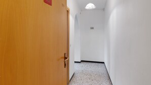 Un corridoio con una porta in legno, un muro bianco, una luce a soffitto e un pavimento decorato.