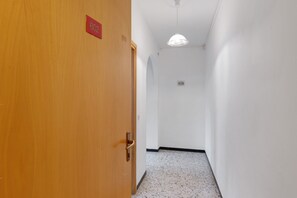 Een gang met een houten deur, een witte muur, een plafondlamp en een doorgaans gestreepte vloer.