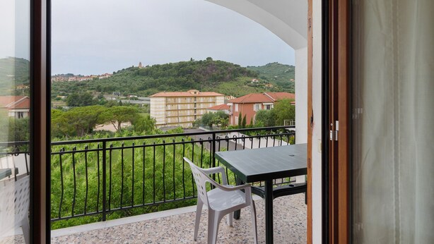 A balcony with a table and chair, overlooking a residential area with houses and greenery. - Apartment '607' with Private Terrace and Shared Garden (Diano Castello)