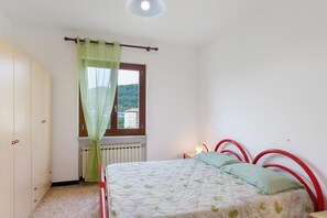 Ein Schlafzimmer mit einem Bett, einem Heizkörper, einem Fenster mit Vorhang und Blick auf eine Hügelkette.
