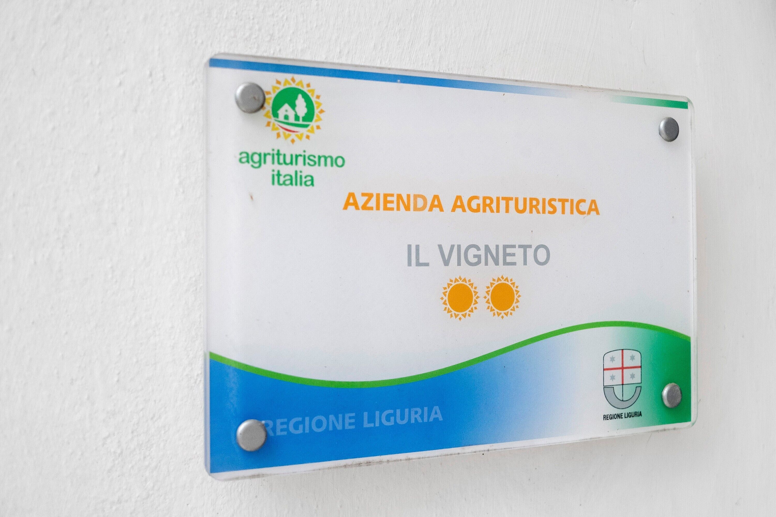 Une enseigne portant les inscriptions « agriturismoitalia » et « AZIENDA AGRITURISTICA IL VIGNETO » indique la présence d’un établissement proposant un séjour à la ferme dans la région de Ligurie.