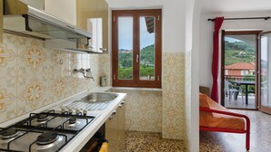 A kitchen with a gas stove, double sink, and a window with a view of greenery. - Apartment '607' with Private Terrace and Shared Garden (Diano Castello)