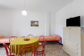 Ein Zimmer mit rundem Tisch, roten Stühlen, einem Bett, einem Fernseher und einem Bild an der Wand.