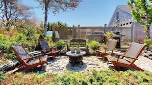 Een terras buiten met een ronde tafel, vier houten stoelen en een houten omheining.