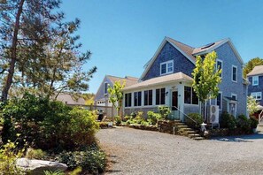 A two-story house with a front porch, a gravel driveway, and a stone wall. - Inviting condo near famed beaches/trails with screened porch & washer/dryer (Provincetown)