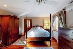 A four-poster bed with a wooden headboard, a nightstand with a lamp, a wardrobe, and a ceiling fan in a bedroom. - Spacious home near the ferry & downtown with enclosed yard, games, & W/D (Tisbury)