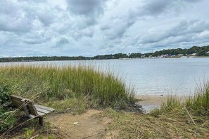 Blick auf einen See mit einer Bank, einer Rasenfläche und Gebäuden in der Ferne.