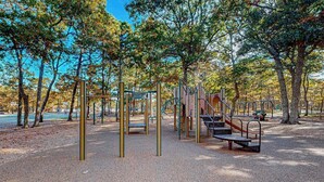 Zona de jocs amb estructures per escalar i tobogan, envoltada d'arbres.