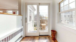 A hallway with a sliding glass door leading to a balcony with a wooden table and chairs. - Historic District Hideaway with Home Office | Walk to Commercial St & Pier (Provincetown)