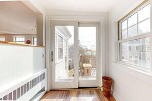 A hallway with a sliding glass door leading to a balcony with a wooden table and chairs. - Historic District Hideaway with Home Office | Walk to Commercial St & Pier (Provincetown)