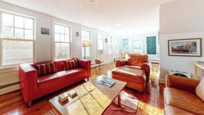 A spacious living room with a red sofa, a brown leather sofa, and a wooden coffee table. - Historic District Hideaway with Home Office | Walk to Commercial St & Pier (Provincetown)