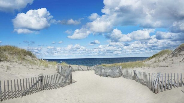 A sandy beach path leading to the ocean, with a wooden fence on both sides. - Historic District Hideaway with Home Office | Walk to Commercial St & Pier (Provincetown)