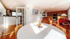 A spacious living area with a round table, a red sofa, and a wooden cabinet. - Historic District Hideaway with Home Office | Walk to Commercial St & Pier (Provincetown)